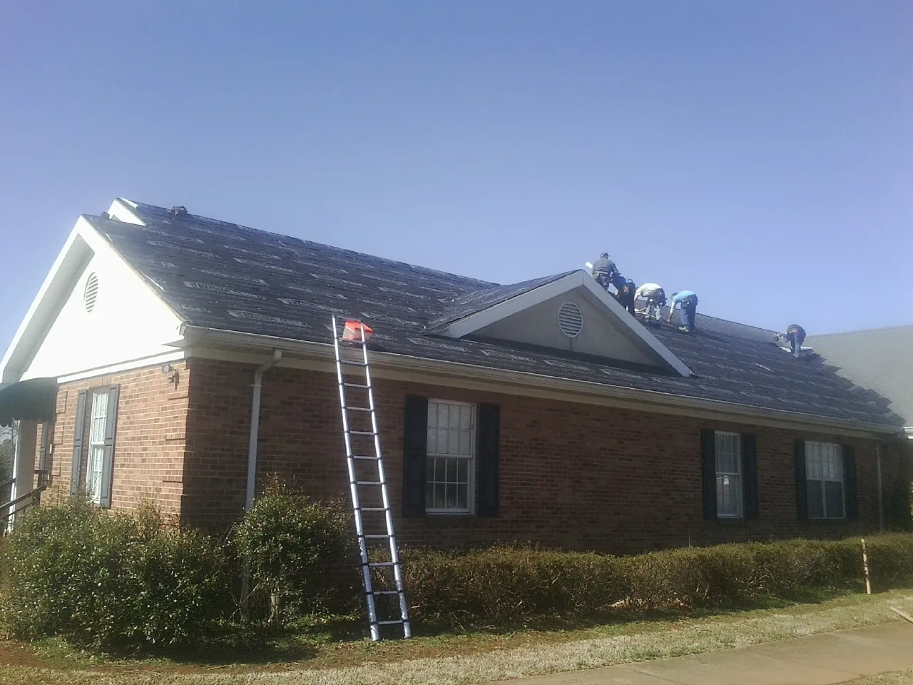 Crew tearing shingles off a brick ranch roof with a ladder set — Emergency Roof Repair work by our crew in Coeymans