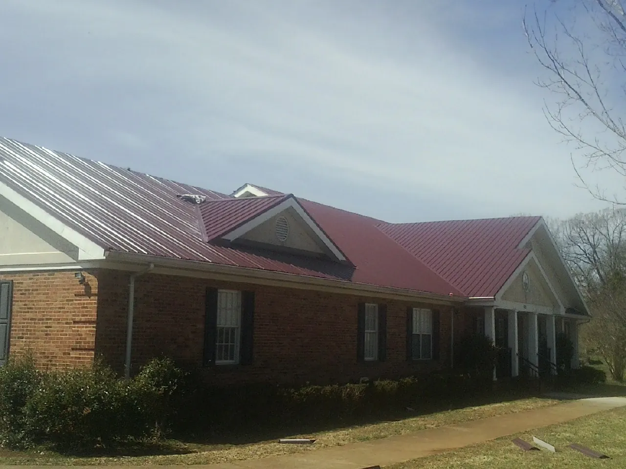 Red metal roof with gabled entries on a long brick building, from a Hail Damage Roof Repair job in Coeymans