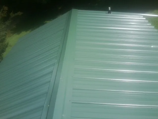 New green metal panels meeting at the ridge of a roof — Flat Roof Repair work by our crew in Coeymans
