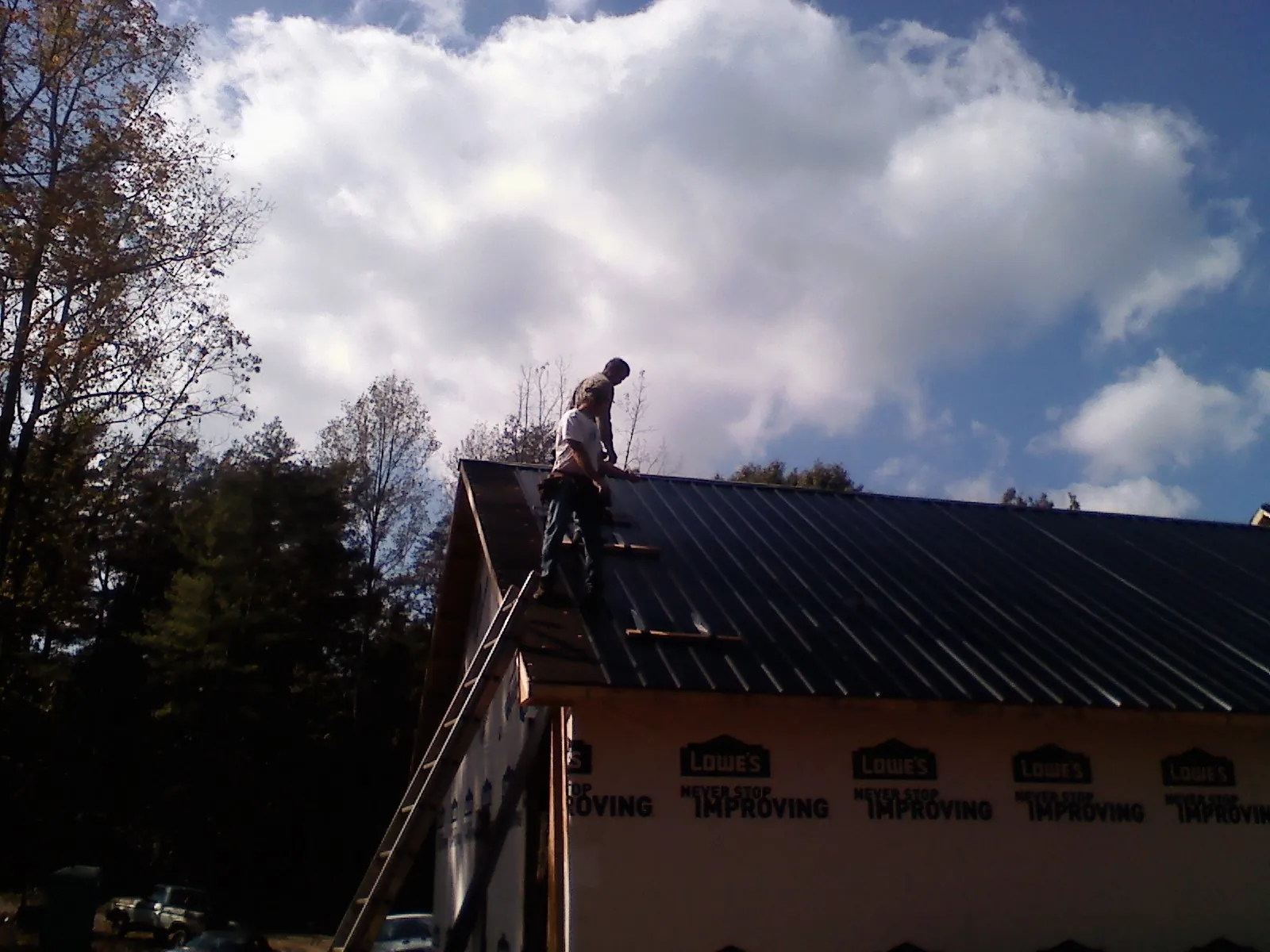 Roofer fastening dark metal panels high against a cloudy sky, from a Roof Inspection job in Coeymans