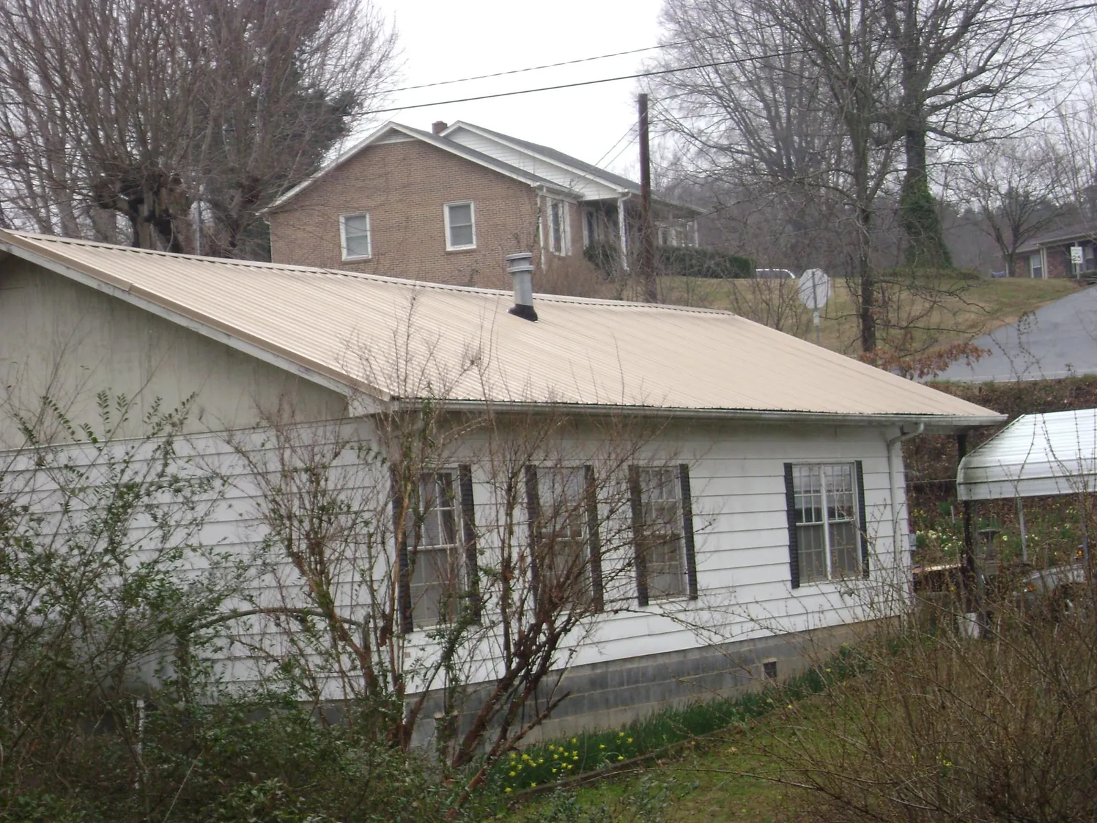 Tan metal roof on a white sided house set into a hillside — Commercial Roofing by Roofing Brothers in Coeymans